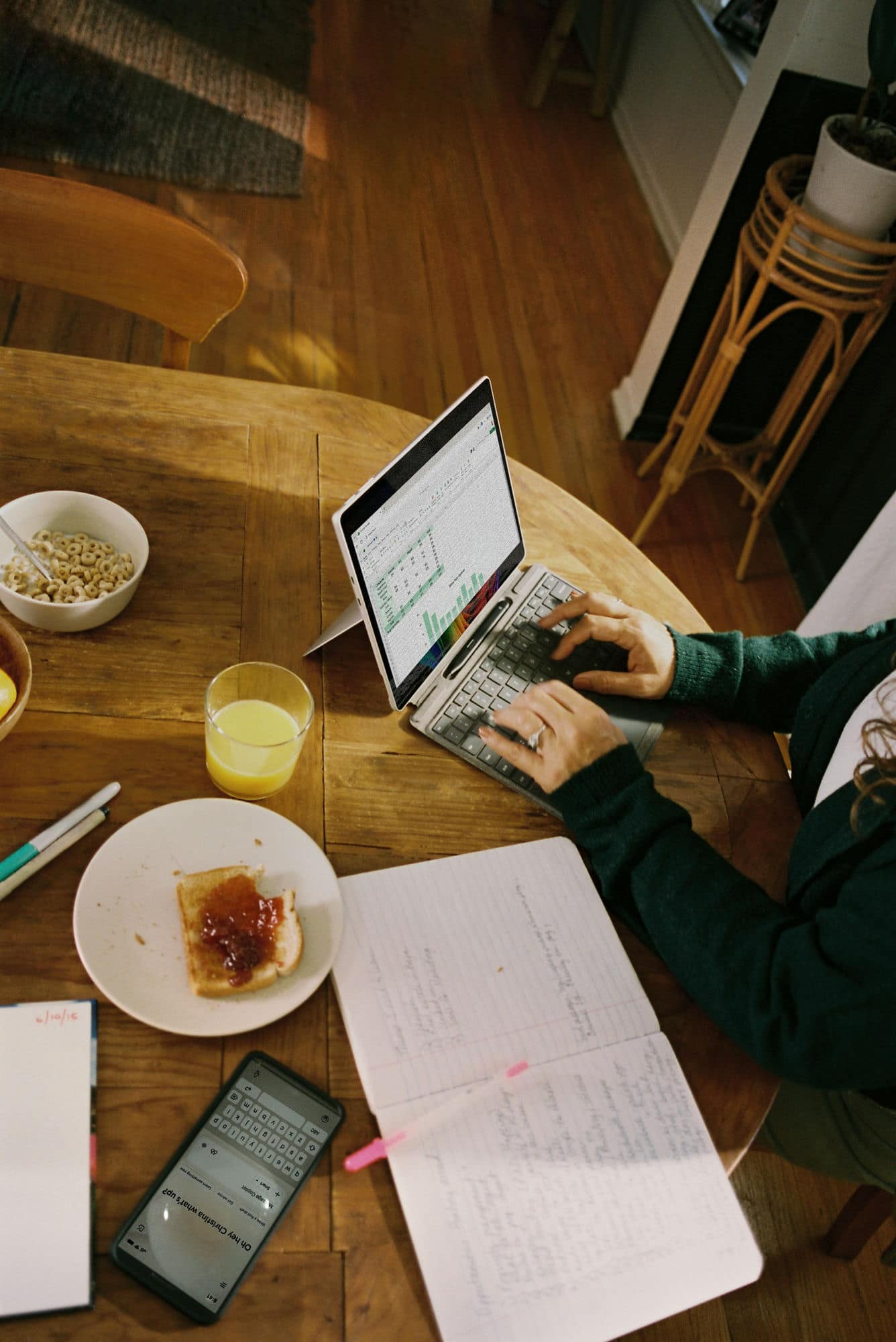 Someone working on a tablet with an AI assistant on their phone at a sunlit breakfast table